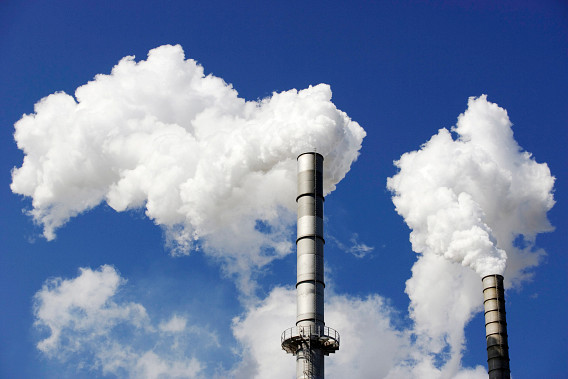 Two industrial smokestacks emitting large plumes of white smoke against a clear blue sky.